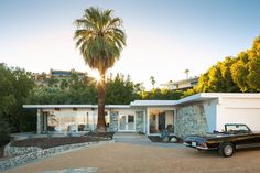 a black car parked in front of a house with a palm tree next to it