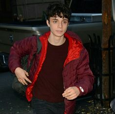 a young man is walking down the street with his hand in his pocket and wearing a red jacket