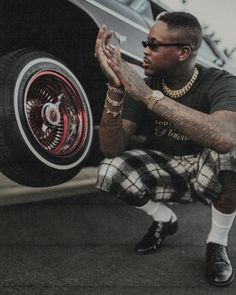 a man sitting on the ground next to a car holding his hands out in front of him