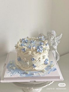 a white cake with blue flowers on it sitting on top of a table next to an angel figurine