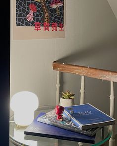 a glass table topped with books next to a painting on the wall and a lamp