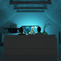 two people sitting on a couch watching tv in a room with blue light coming from the ceiling