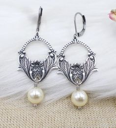 These elegant handmade earrings feature beautiful cream imitation pearls and a vintage-inspired antique silver plated brass flower design. The chandelier-style earrings hang 2.25 inches long and are perfect for adding a touch of nature and art to any outfit. The beaded and dangle/drop style of the earrings make them a great choice for weddings and Mother's Day gifts. The lever back closure ensures that the earrings will stay securely in place on the lobe. The earrings are silver plated and feature glass material. These earrings are not only unique and beautiful, but also affordable. Add a retro and fashion-forward touch to your jewelry collection with these stunning earrings from Jewelry518. Art Noveau Jewelry, Silver Art Nouveau Jewelry For Wedding, Art Nouveau Pearl Jewelry, Art Nouveau Hallmarked Jewelry Gift, Art Nouveau Dangle Earrings Gift, Nickel-free Art Nouveau Earrings As Gift, Pearl Art, Art Nouveau Earring, Art Nouveau Silver