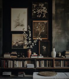 there are many pictures on the wall above this bookshelf with flowers in vases