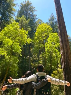 two people standing in the woods with their arms outstretched