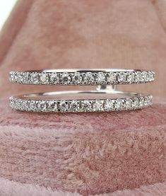 two white gold wedding rings with diamonds on top of pink furnishing, close - up