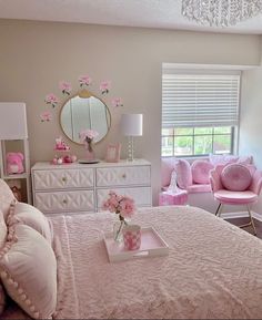 a bedroom decorated in pink and white with flowers on the bed, dresser, mirror, and chair