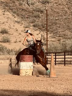 a woman riding on the back of a brown horse next to a wooden pole in an open field