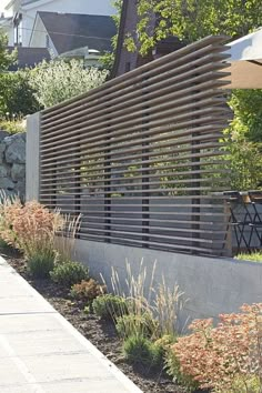 a wooden slatted fence in front of a building with plants and flowers on the side