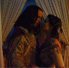 a man and woman dressed in medieval clothing kissing each other while standing next to curtains