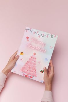 someone holding up a christmas card on top of a pink background