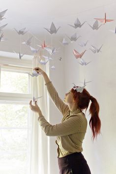 a woman is hanging origami birds from the ceiling