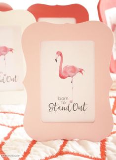 two pink flamingos sitting on top of a bed next to a white frame with the words born to stand out