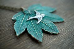 a green leaf with a bird on it is sitting on a wooden table and has a chain attached to it