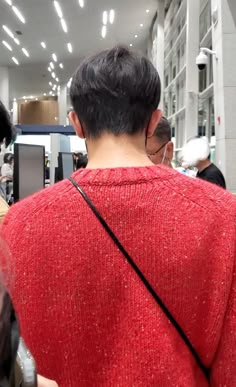 the back of a woman's red sweater in an airport terminal with people walking around