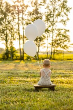 a little boy sitting on a bench holding three white balloons