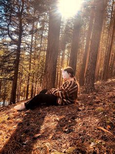 a woman sitting on the ground in front of trees with sun shining through her eyes