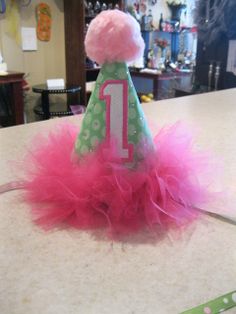 a pink and green birthday hat with the number one on it sitting on top of a table