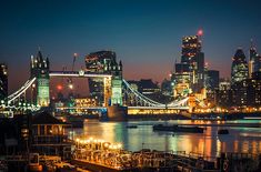 the city skyline is lit up at night, with boats docked on the river below