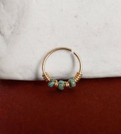 a gold ring with turquoise beads on it sitting on top of a red velvet bag