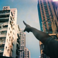 a person pointing at the sky in front of tall buildings