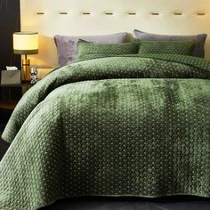 a bed with green bedspread and pillows in a room next to a lamp