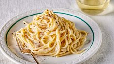 a white plate topped with pasta covered in sauce next to a glass of wine and a fork