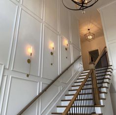 the stairs are lined with white paneling and light fixtures, along with two chandeliers