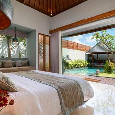 a bed sitting next to a large window in a bedroom under a wooden ceiling fan