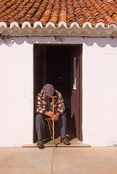 a man sitting in front of a doorway with a cane and hat on his head