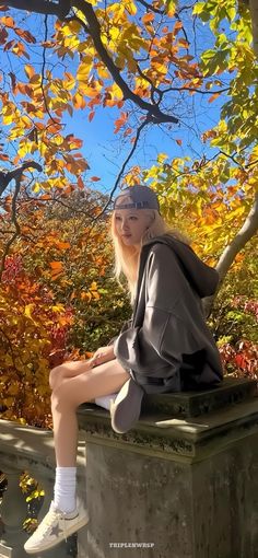 a woman sitting on top of a cement bench next to a tree filled with leaves