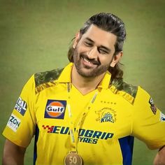 a man with long hair wearing a yellow shirt and gold medal in front of a green background