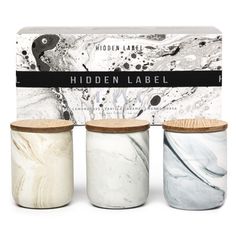 three jars with labels on them sitting in front of a white box filled with black and white marble