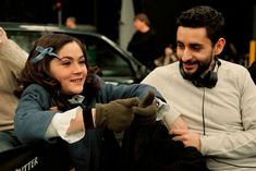 a man and woman sitting next to each other in front of a car with headphones on