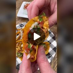 a person holding up a tortilla with toppings on it and another hand reaching for the food