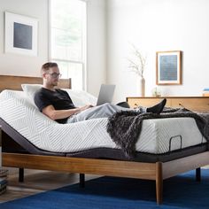 a man is sitting on his bed with a laptop in front of him and looking at the screen