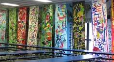 an empty classroom with desks covered in colorful papers and graffiti on the wall behind them