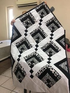 a person holding up a black and white quilt on a table with an air conditioner in the background