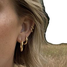 a woman wearing large gold hoop earrings in front of her face with grass behind her