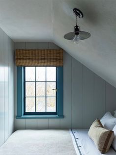 a bed sitting under a window in a bedroom next to a wall mounted light fixture