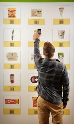 a man standing in front of a white wall holding a cell phone up to his ear