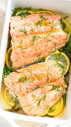 two salmon fillets in a white dish with lemons and herbs