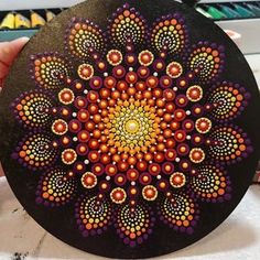 a person holding up a black plate with orange and purple designs on the inside of it