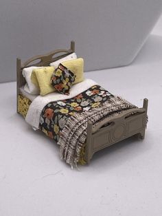 a small dollhouse bed with a blanket and pillows on it's headboard