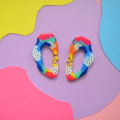 two pairs of colorful earrings sitting on top of a multicolored surface with different shapes and sizes