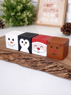 three wooden blocks with faces on them sitting on top of a piece of wood next to pine cones