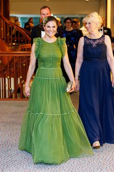 two women in green dresses are walking down the carpeted hall with other people behind them