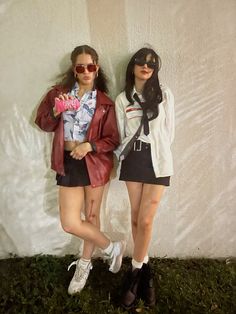 two young women standing next to each other in front of a white wall with grass