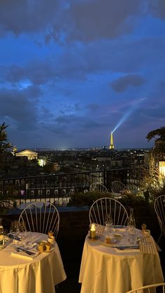 two tables with white tablecloths are set for dinner overlooking the city at night