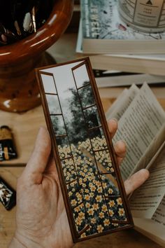 a person holding an open book on top of a wooden table with flowers in it